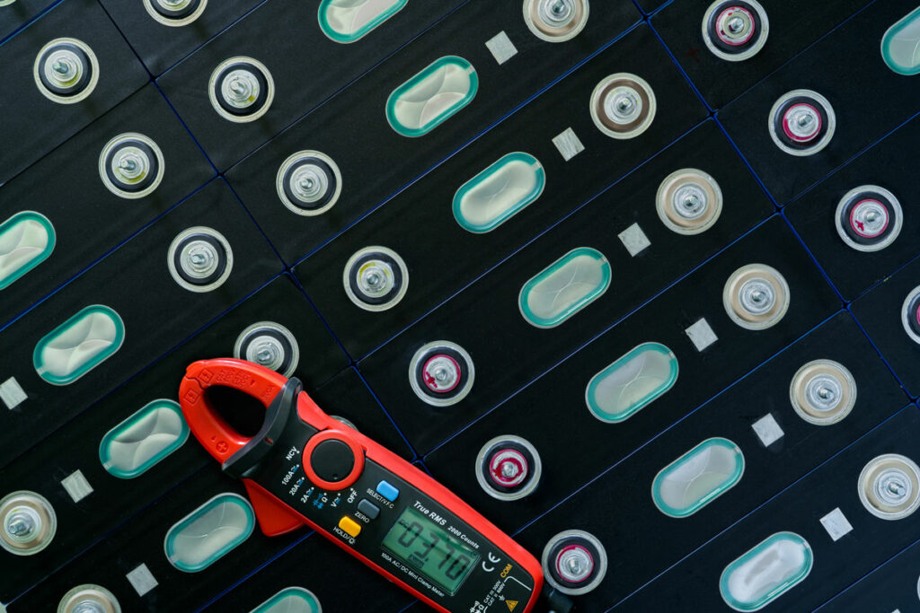 auto lithium battery close up with a calibrating device laying on it. the device is red with a green led screen and a couple of buttons