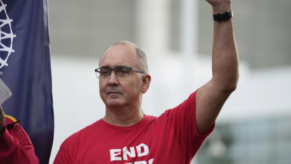 wearing a red t shirt - uaw president shawn fain raises his fist in solidarity with workers