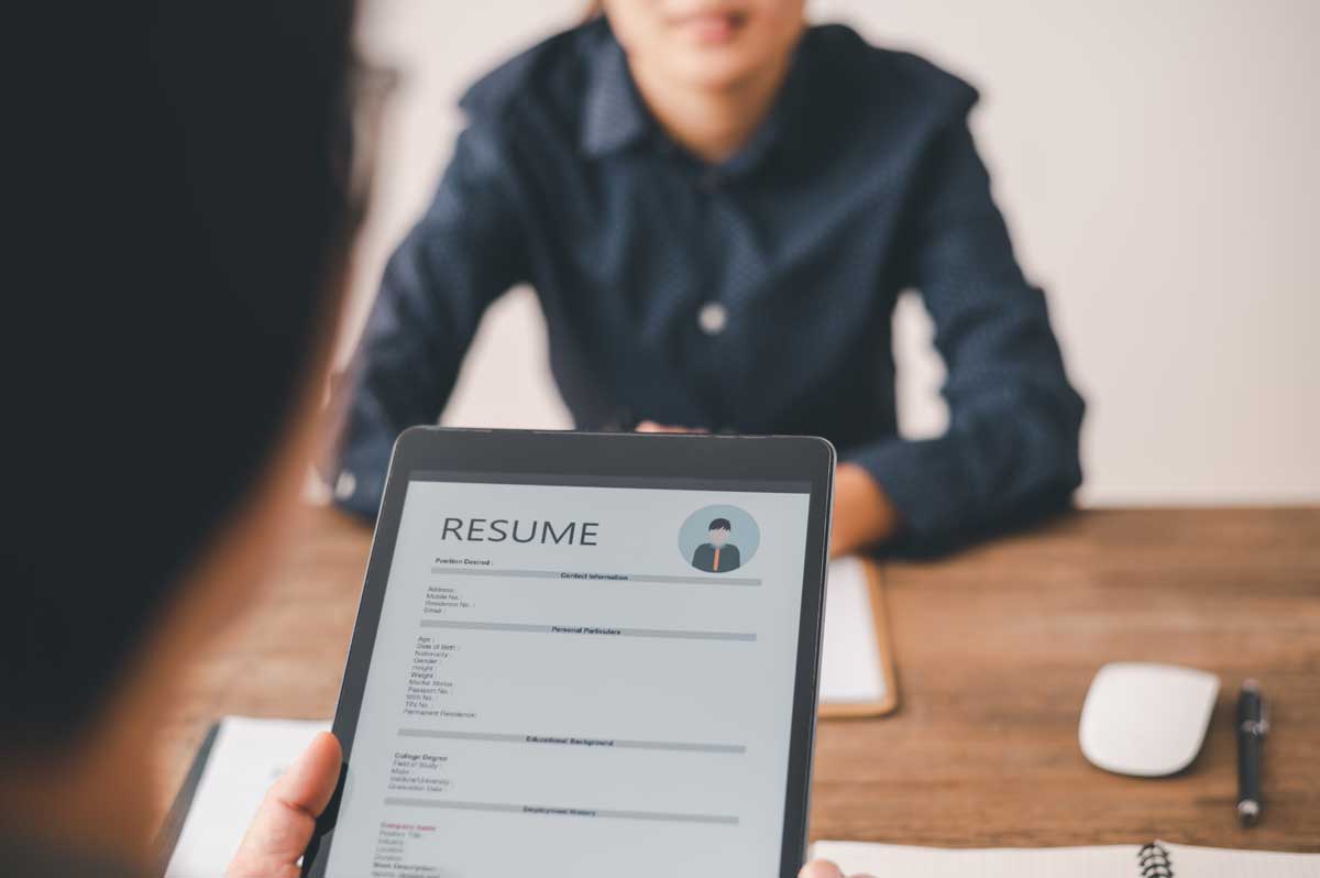 picture of a resume on a clipboard being viewed by point of view. male with hands folded on table in blue shirt is softly focused in the background